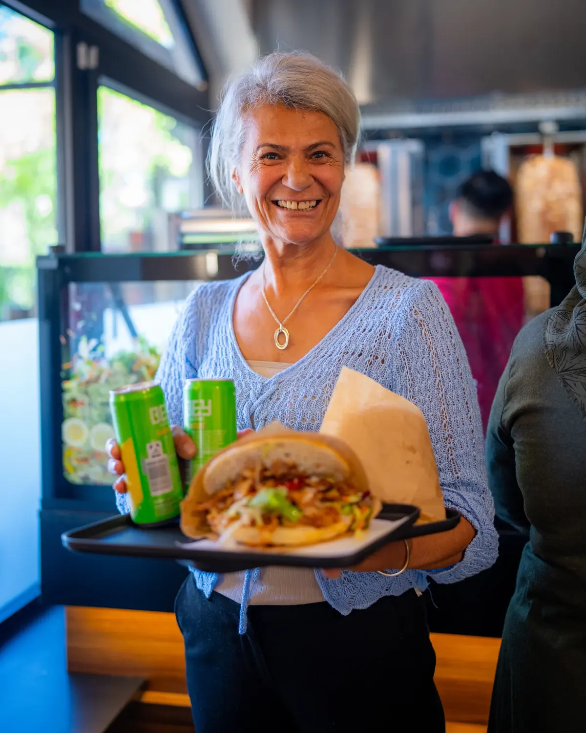 Lächelnde Kundin mit Döner-Tablett und Getränken bei Amca's Kebab