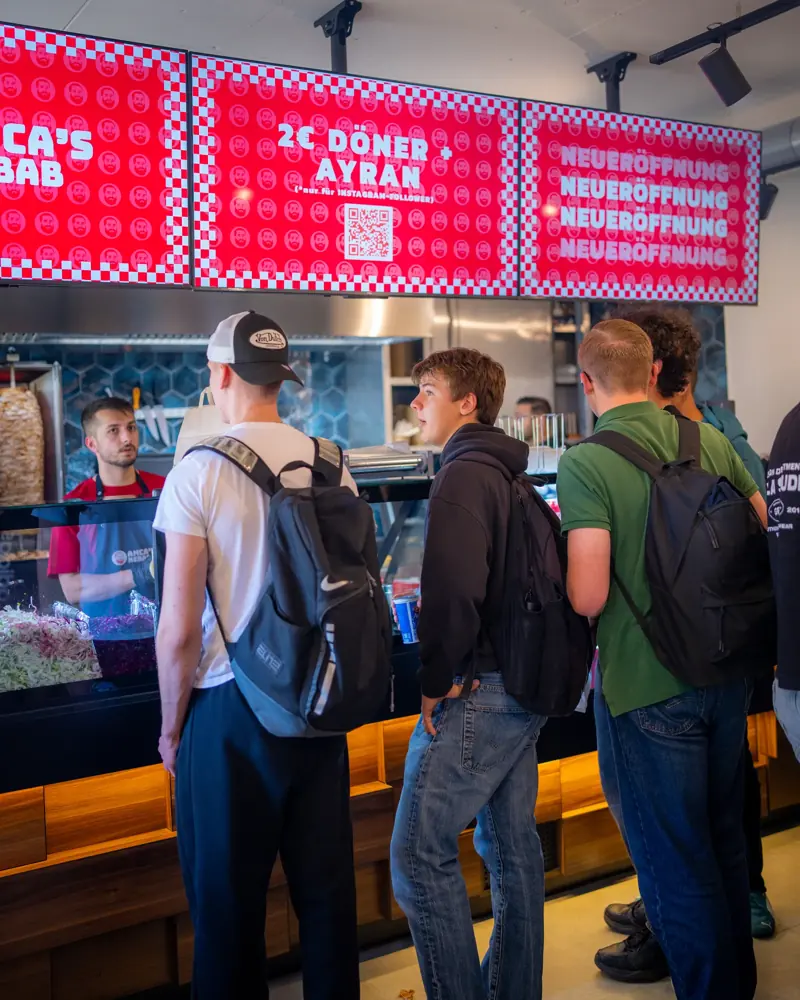 Lange Schlange vor der Theke mit roten Menütafeln bei Amca's Kebab
